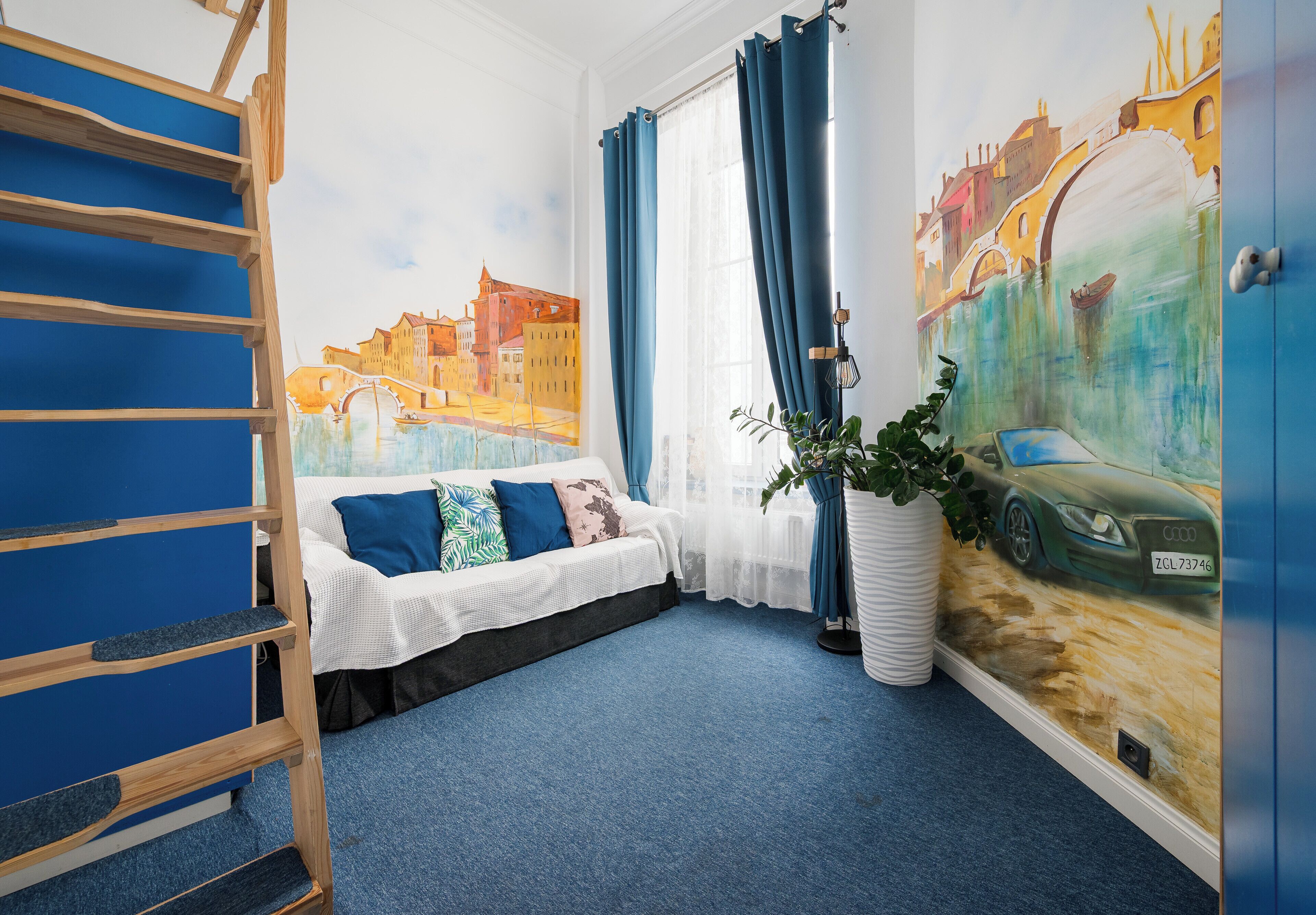 Um quarto com cama beliche, sofá com almofadas, janela grande com cortinas, uma planta e um mural retratando um horizonte urbano e um carro.