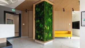 A reception area with a moss wall, a wooden slatted ceiling, a yellow bench, and a white reception desk. - Cracow Novum Apartment #533 (Kraków)