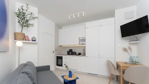 A modern living room with a grey sofa, a small blue table, and a kitchen area with white cabinets and a flat-screen TV. - Cracow Novum Apartment #533 (Kraków)