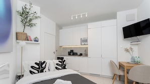 A modern hotel room with a bed, a desk, a chair, a TV, a small kitchen area, and a potted plant. - Cracow Novum Apartment #533 (Kraków)