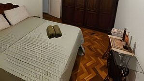 A bedroom with a bed, a wooden wardrobe, a ceiling fan, and a small table with a lamp. - 3 Minutos da Praia - Prime Location (Rio de Janeiro)