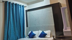 A modern bedroom with a bed, blue curtains, a ceiling fan, and recessed lighting. - Hotel Origin (Guwahati)