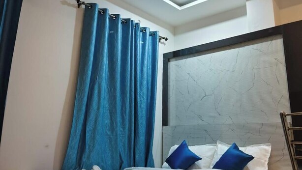 A modern bedroom with a bed, blue curtains, a ceiling fan, and recessed lighting. - Hotel Origin (Guwahati)