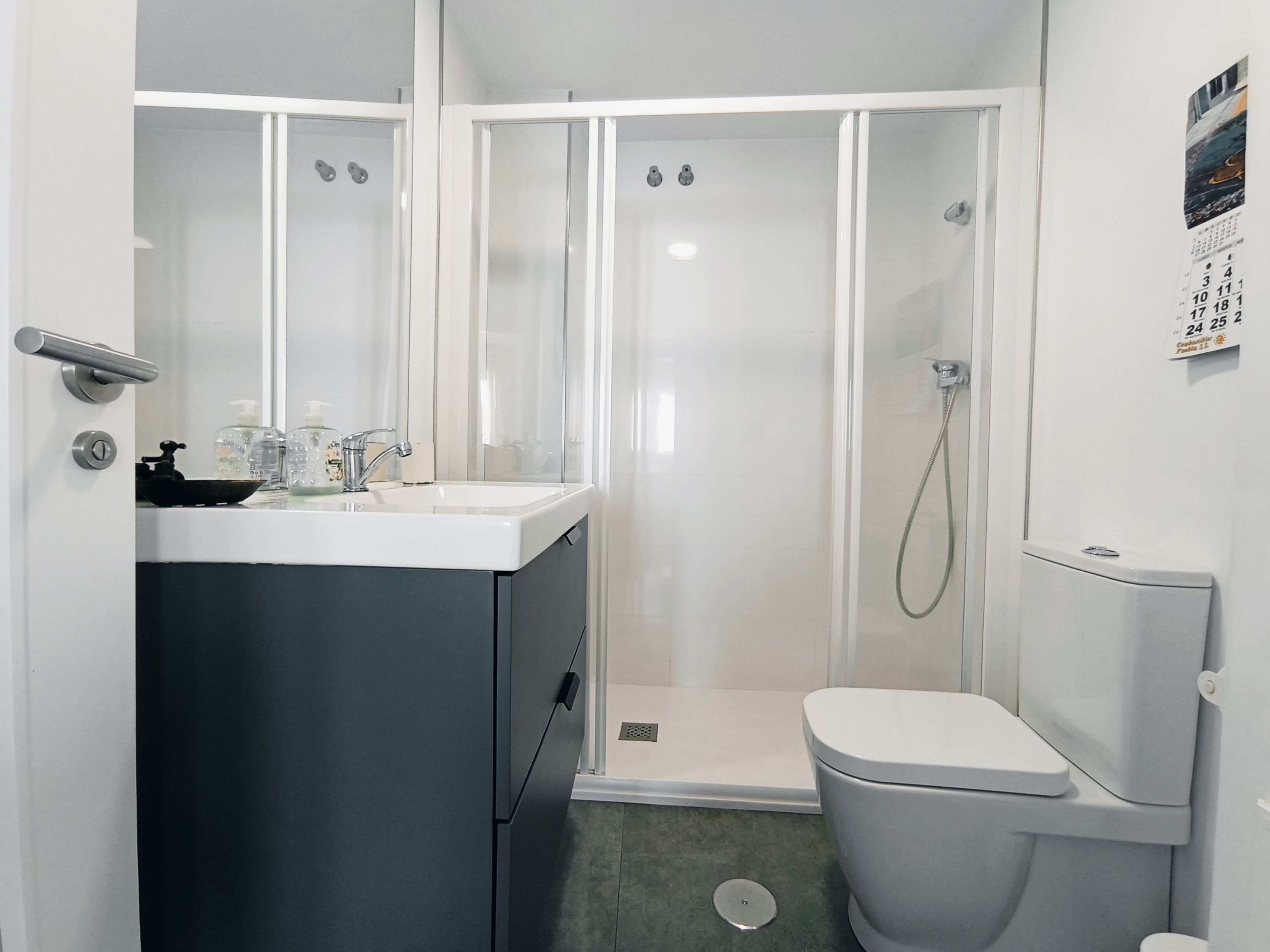 A compact bathroom with a white sink, a toilet, and a glass-enclosed shower.