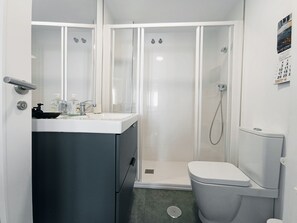 Ein kleines Badezimmer mit einem weißen Waschbecken, einer Toilette und einer Duschkabine.