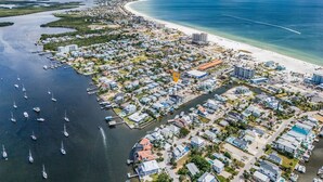 Ett flygbildsbild av ett bostadsområde vid kusten med en småbåtshamn, hus och en strand.