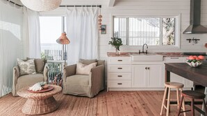 Una cocina acogedora con comedor, que cuenta con piso de madera, armarios blancos, un ventanal grande y una lámpara colgante.