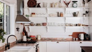 Una cocina con muebles blancos, encimera de mármol y diversos utensilios de cocina en estantes.