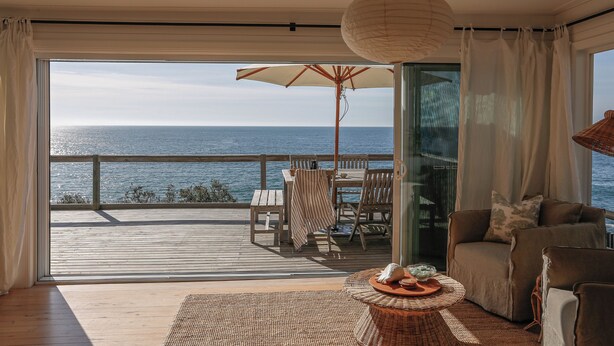 Una habitación con vista al mar, una terraza de madera, una mesa con sillas, un sofá y una lámpara colgante.