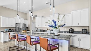 Una cocina moderna con armarios blancos, encimera de granito y una isla central con taburetes de bar.