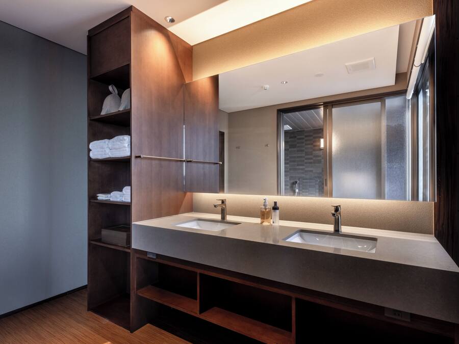 A modern bathroom with two sinks, a large mirror, and wooden shelving with towels.