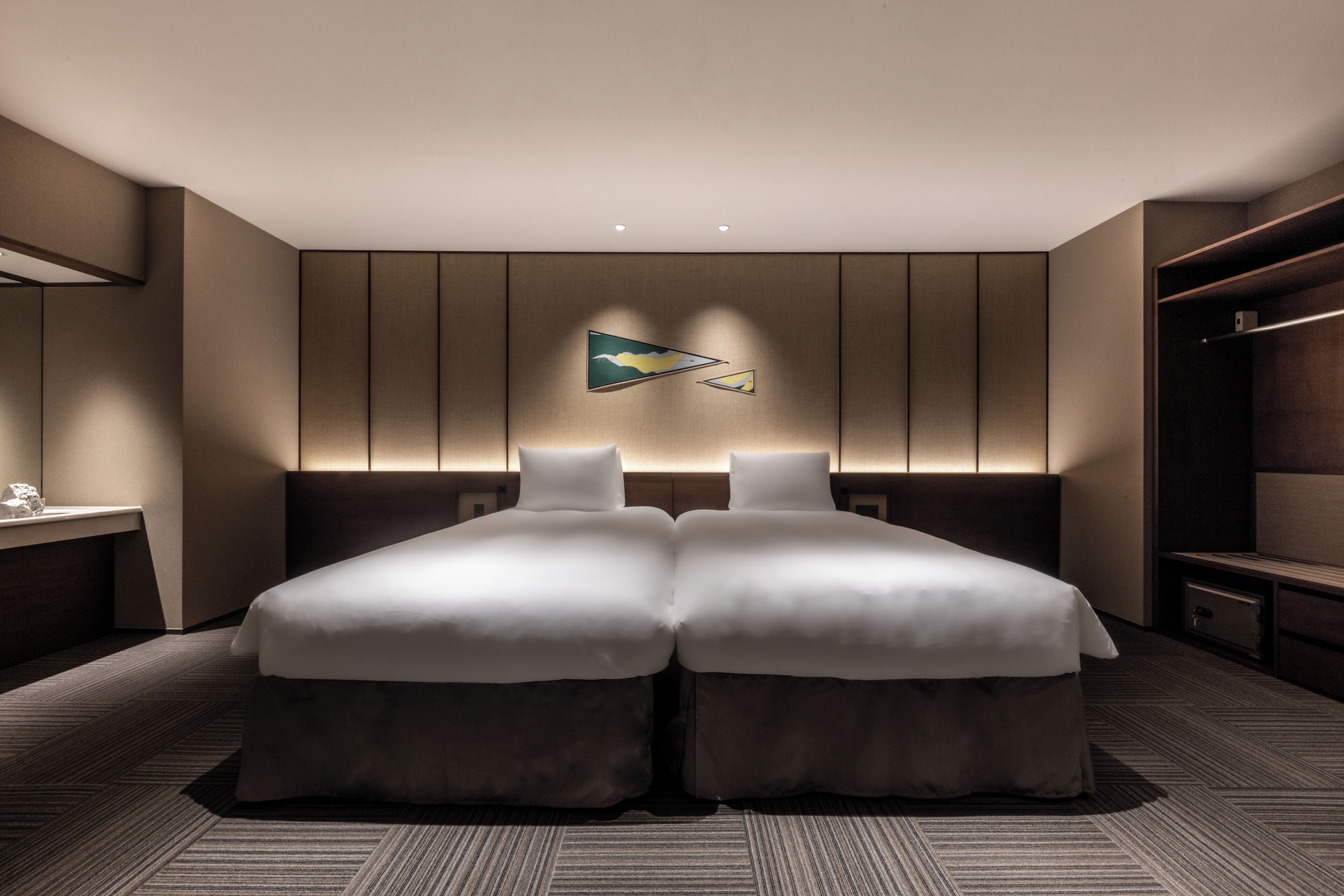 A modern hotel room with two beds, a nightstand, and a wardrobe.
