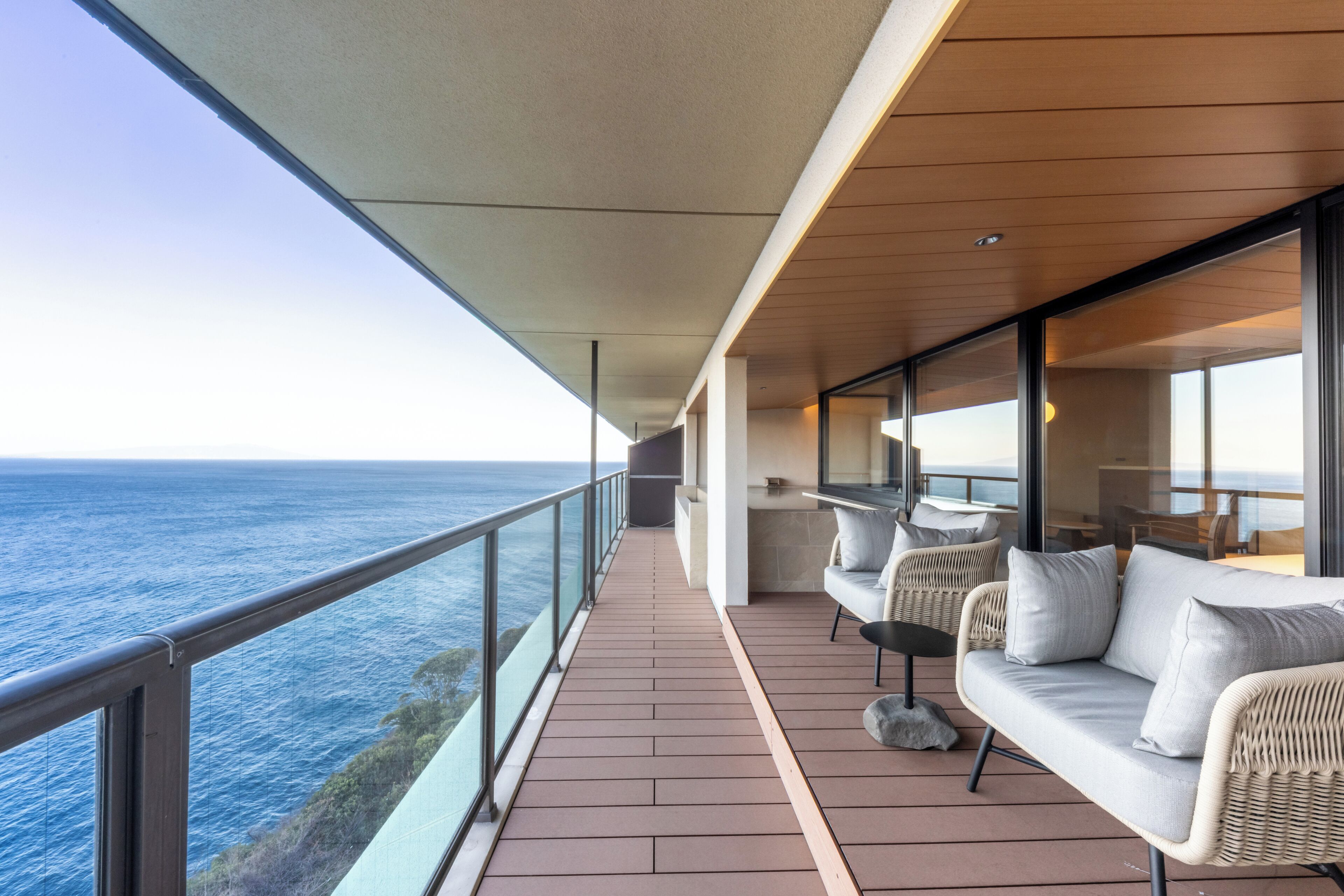 A balcony with a view of the ocean, furnished with a sofa and chairs, and a glass railing.