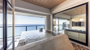 Une piscine à débordement moderne offrant une vue dégagée sur l’océan, un espace salon avec un canapé et une table, ainsi qu’une grande fenêtre donnant sur la mer.