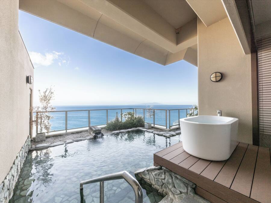 A modern bathroom with a large bathtub, a small pool, and a view of the ocean.