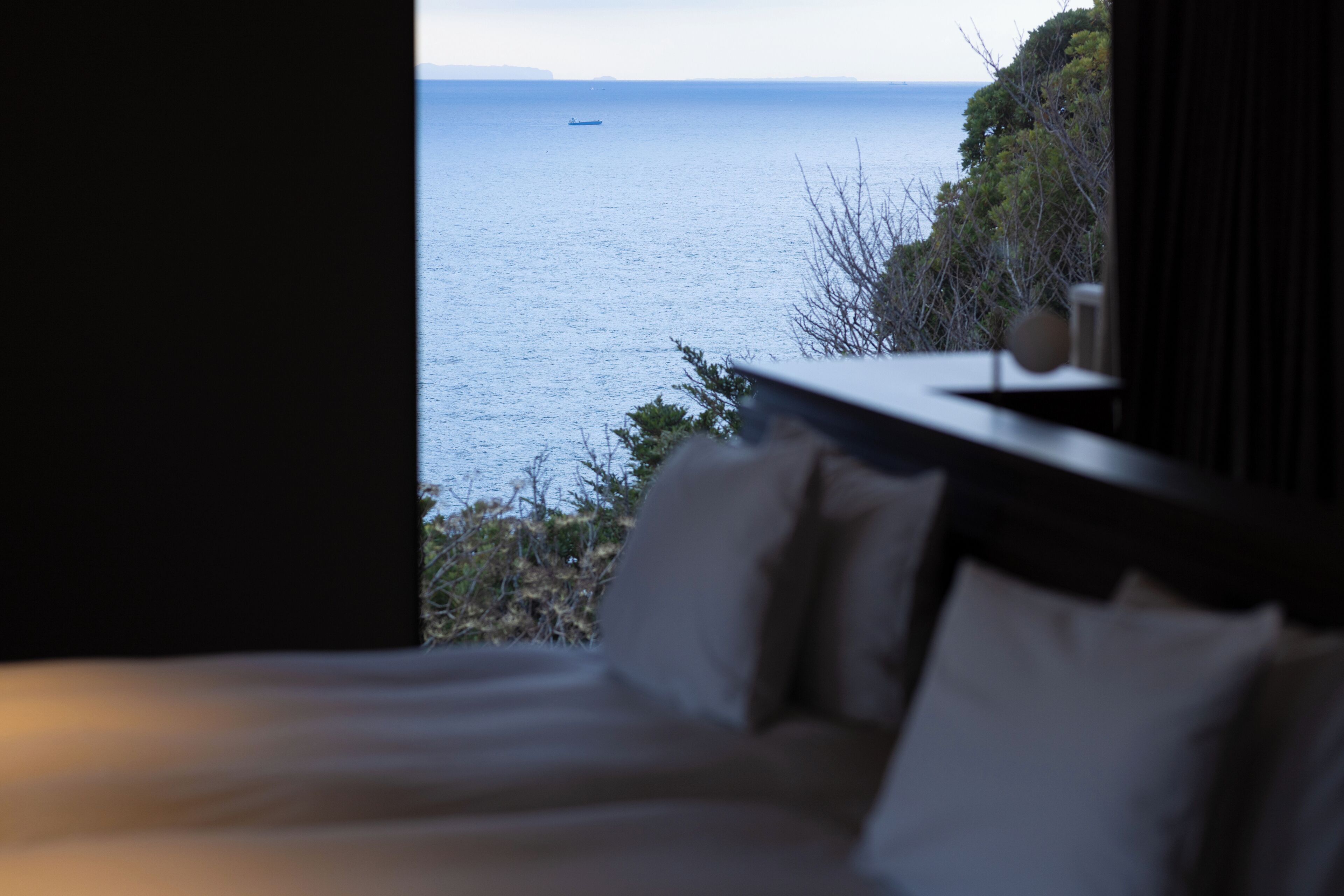 A bedroom with a view of the sea and a ship in the distance.