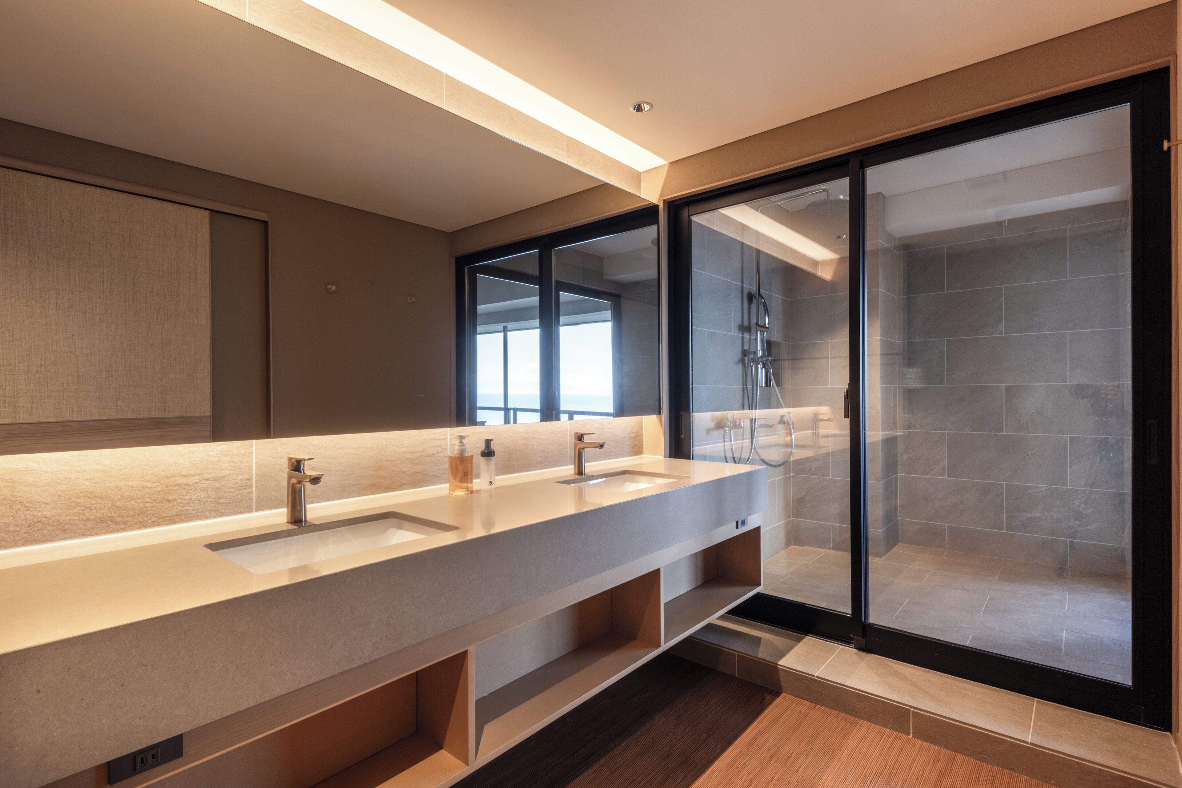 A modern bathroom with a long vanity, two sinks, and a glass-enclosed shower area.
