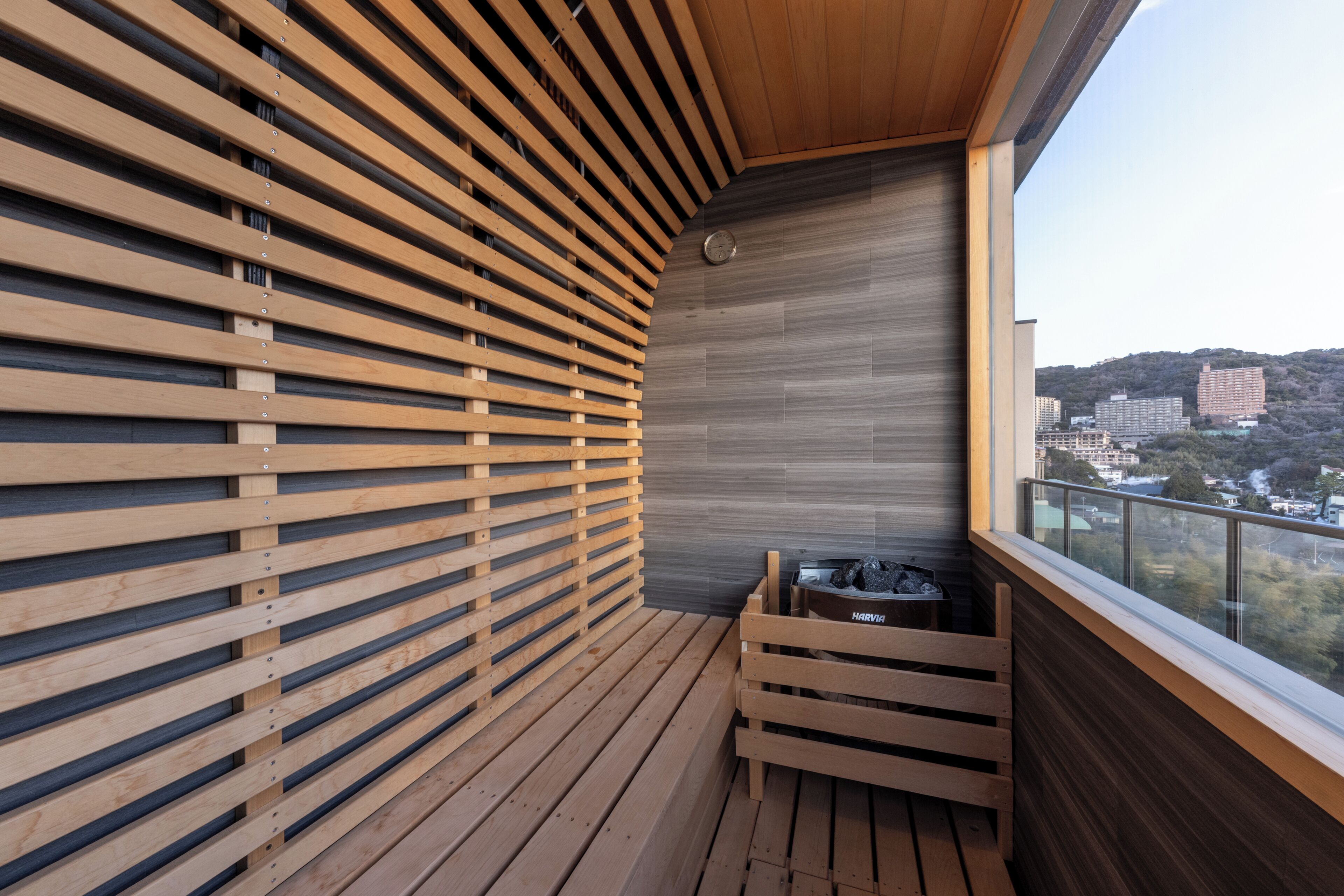 A balcony with wooden slats, a small seating area, and a view of buildings in the distance.
