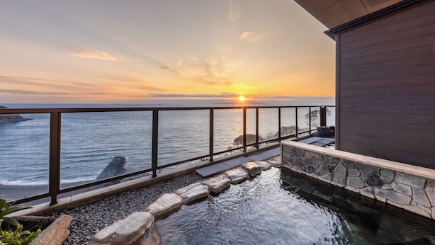 Une vue sur le coucher de soleil depuis un balcon, avec une piscine bordée de pierres et un bâtiment en bois.