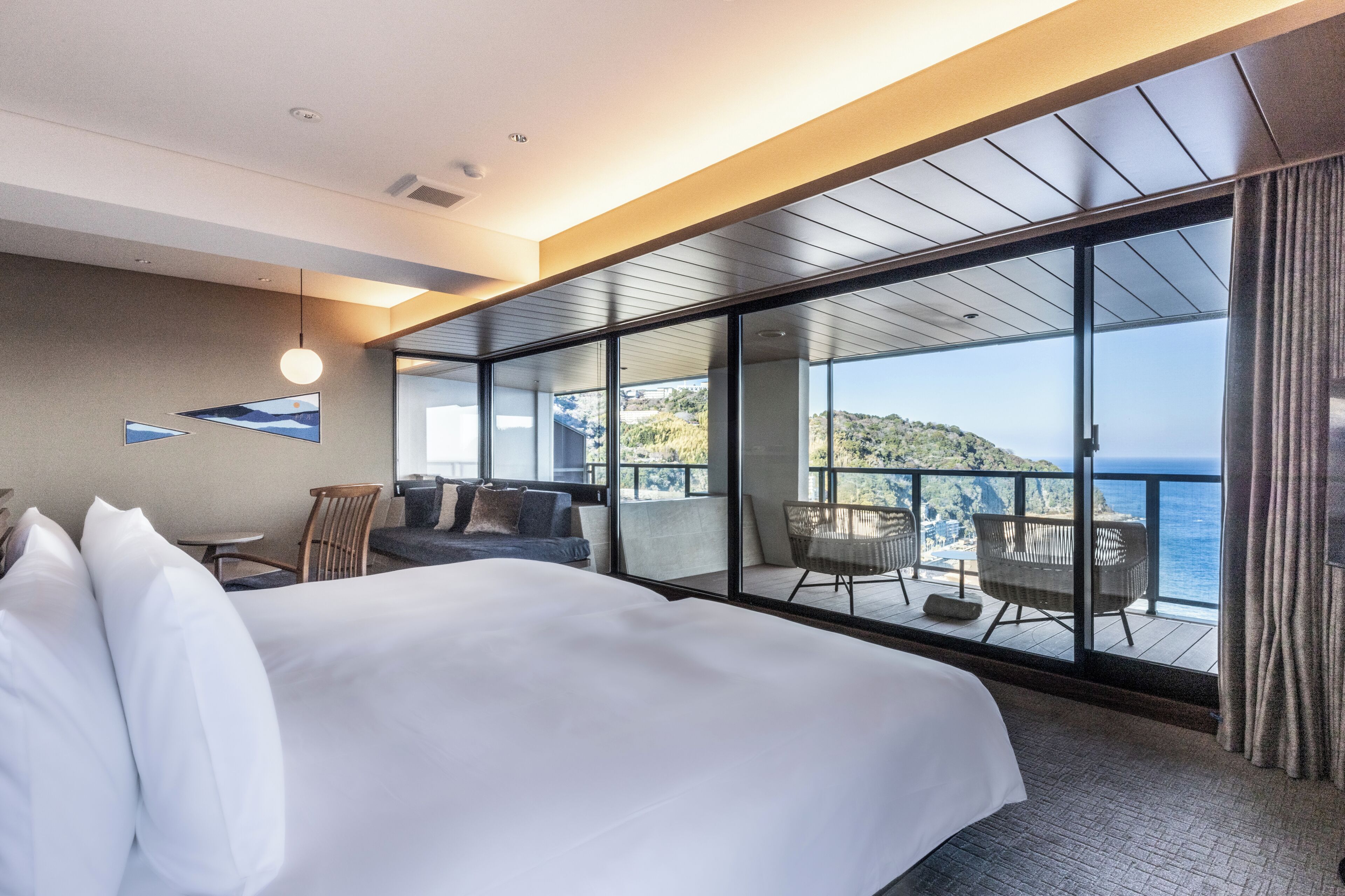 A hotel room with a large bed, a balcony with seating, and a view of the sea.