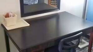 Ett mörkt skrivbord i trä med en vit bricka som innehåller pennor och blyertspennor. En spegel är monterad ovanför skrivbordet och reflekterar en del av rummet.