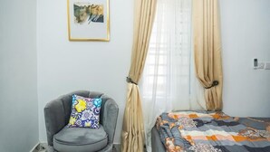 A room with a bed, a chair, a framed picture on the wall, and beige curtains. - Relax By Water-View 1-Bed-APT  With 24HRS PWR+ Wi-Fi (Lagos)