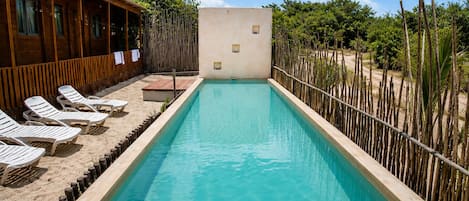 A rectangular pool with a wooden deck and lounge chairs, surrounded by a bamboo fence and vegetation.