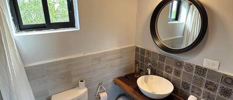 A bathroom with a toilet, sink, mirror, and a window.