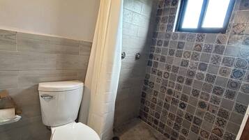A bathroom with a toilet, shower, and a small window.