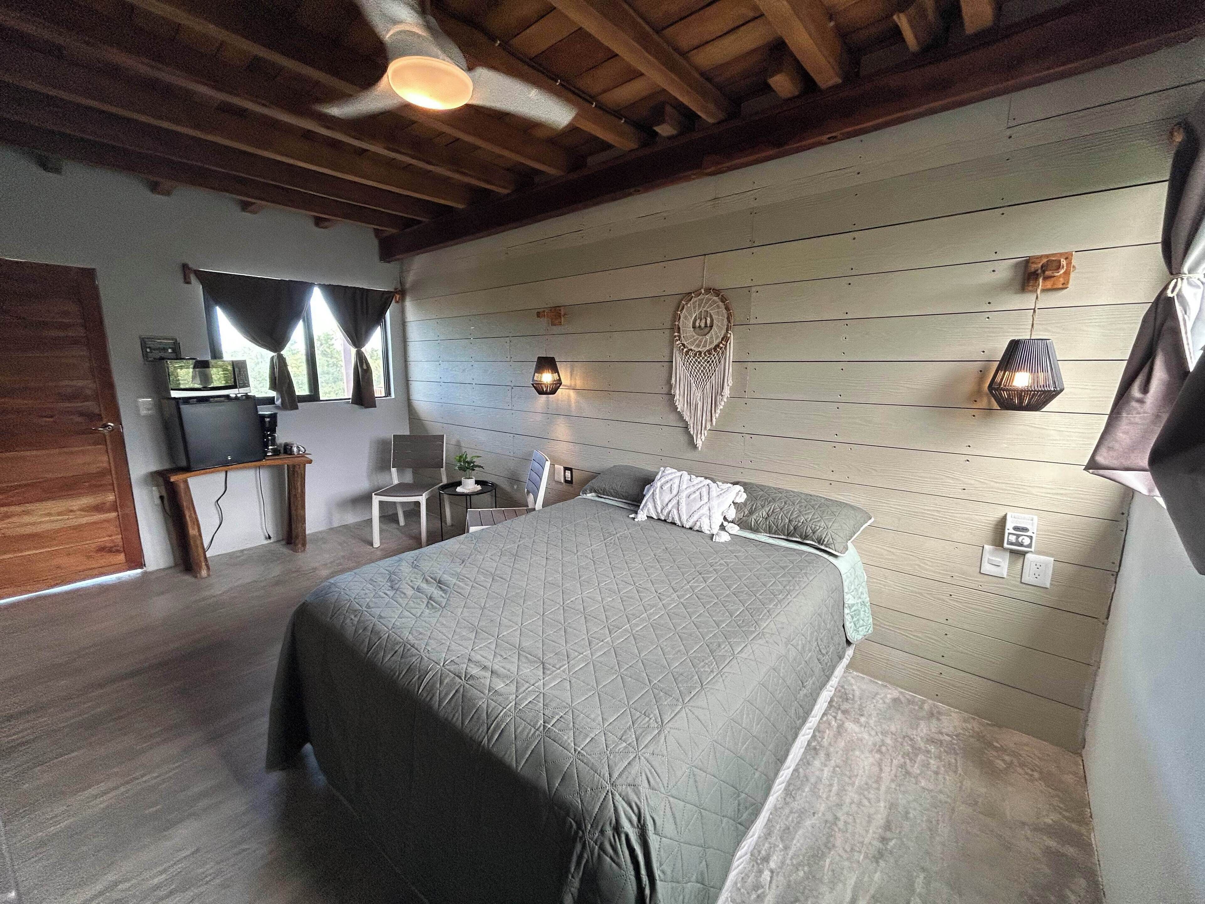 Een slaapkamer met een bed, een bureau, een stoel, een wandlamp en een plafondventilator.