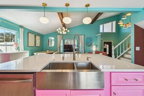Una cocina con isla central, pileta de acero inoxidable y muebles color rosa.