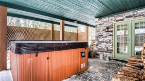 Un bain à remous sous une pergola en bois, avec un mur en pierre et une porte verte.