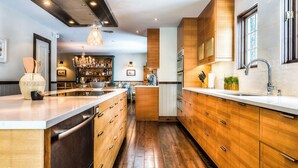 Une cuisine moderne avec des meubles en bois, un îlot central et un coin bar à l’arrière-plan.