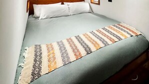 A bedroom with a bed, a wooden headboard, a green wall, and a patterned throw blanket.