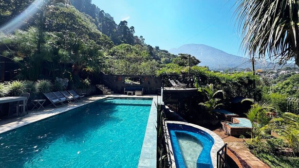 A pool with lounge chairs and a view of a mountainous landscape.