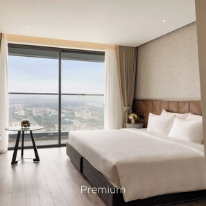 Een hotelkamer met een groot bed, een kleine tafel met een vaas, en een uitzicht op een stadsbeeld door een groot raam.