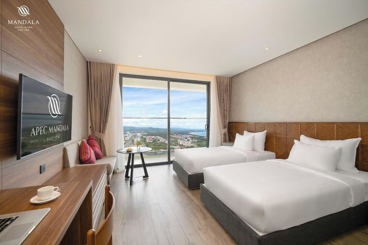 Habitación de hotel con dos camas, televisión, escritorio y vistas a la ciudad.