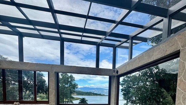 Ein modernes Zimmer mit Glasdecke, Blick auf einen See, einer eingebauten Sitzbank mit Kissen und einem kleinen Tisch mit Stuhl.