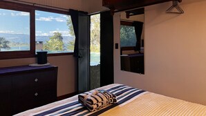 Ein Schlafzimmer mit Bett, Kommode, Fenster mit Aussicht und Spiegel.
