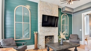 A living room with teal walls, a stone fireplace, a flat-screen TV, and leather furniture. - Large Milwaukee Home • 4BR • Fast WiFi (Milwaukee)