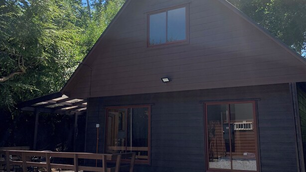 A wooden cabin with a large window, a porch, and a gravel driveway. - Cabañas El Nativo 2 - Licán Ray (Villarrica)
