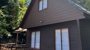 A two-story house with a sloped roof, wooden siding, and a covered porch with a railing. - Cabañas El Nativo 2 - Licán Ray (Villarrica)