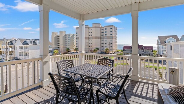 A covered outdoor area with a table and chairs, overlooking a residential area with multiple buildings. - Sleeps 44! Walk to Beach • Private Pool • BBQ (North Myrtle Beach)