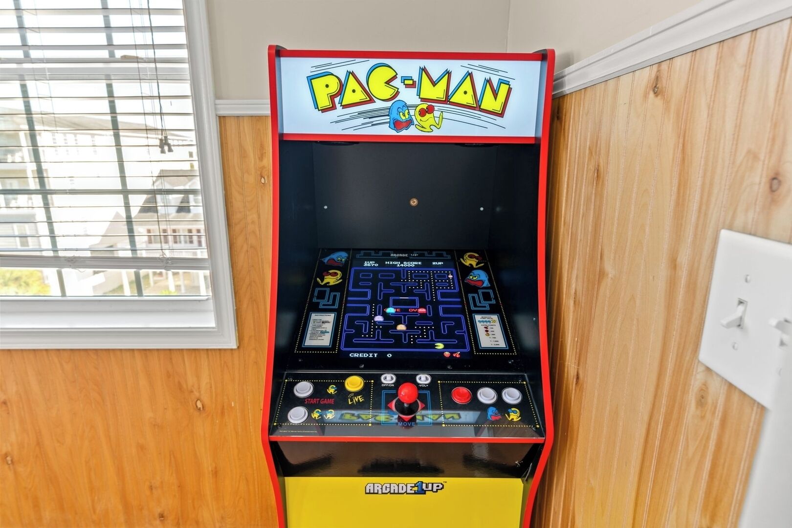 A Pac-Man arcade machine with a yellow base and a red top, featuring a maze game and control buttons.