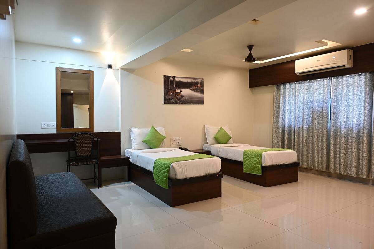 A hotel room with two beds, a desk, a chair, a bench, an air conditioner, and a painting on the wall.