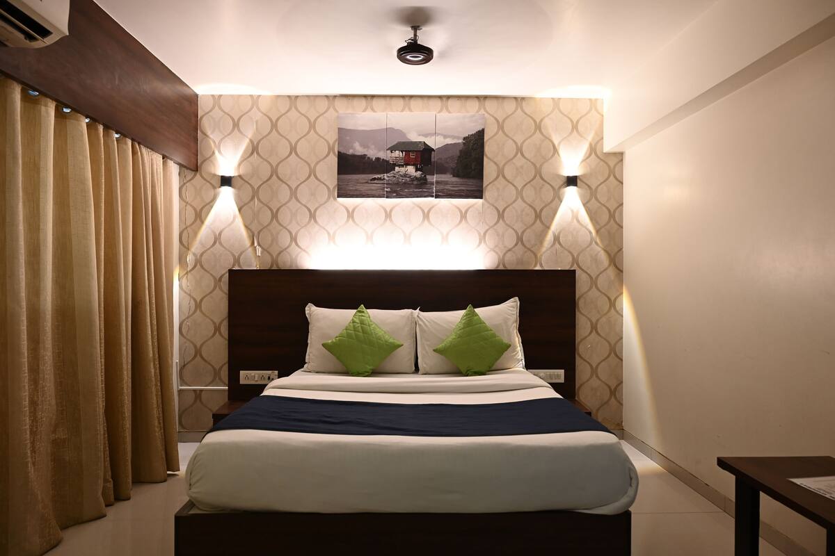 A hotel room with a bed, curtains, a wall-mounted picture, and two wall sconces.
