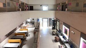 A spacious indoor area with multiple seating options, including tables and benches, and a kitchen area in the background. - Hotel Express Airoli (Navi Mumbai)