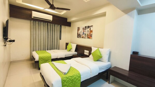 Habitación de hotel con dos camas, ventilador de techo, aire acondicionado y televisor en la pared.