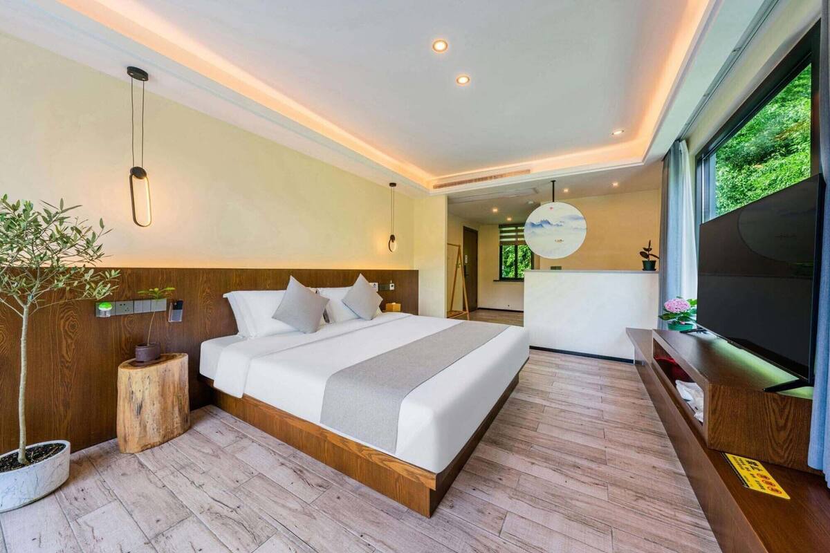 Camera da letto moderna con un letto grande, una testiera in legno, comodini, una TV e vista sul verde.