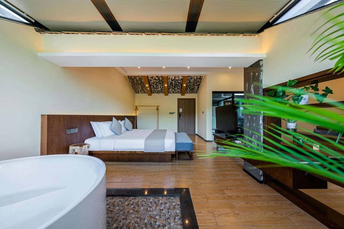 Una camera d'albergo moderna con un letto grande, un'area salotto separata, una vasca da bagno e vista esterna.